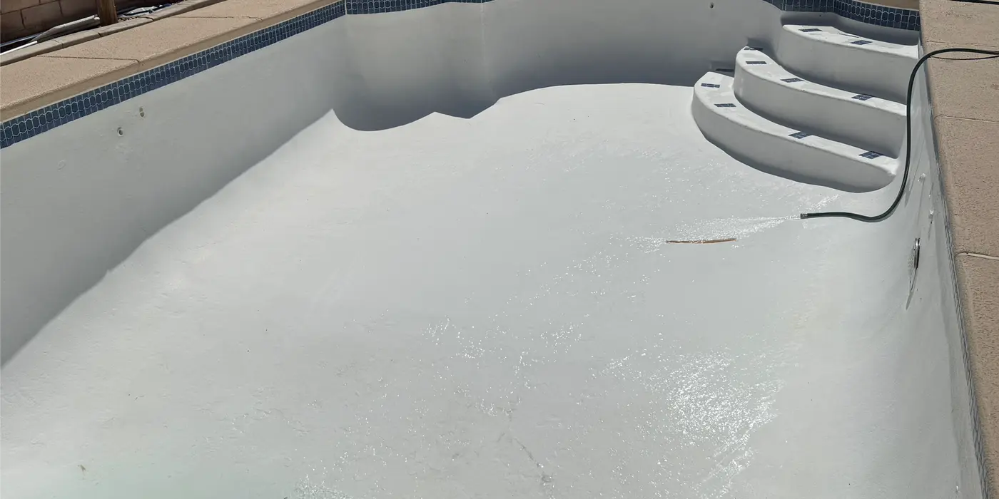 Drained pool with freshly acid-washed white plaster and a hose refilling it